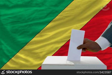 man putting ballot in a box during elections in front of national flag of congo