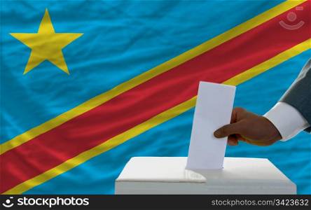 man putting ballot in a box during elections in front of national flag of congo