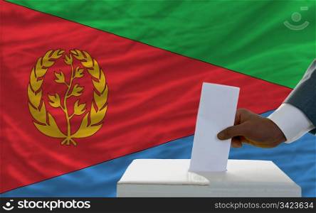 man putting ballot in a box during elections in front of national flag of eritrea