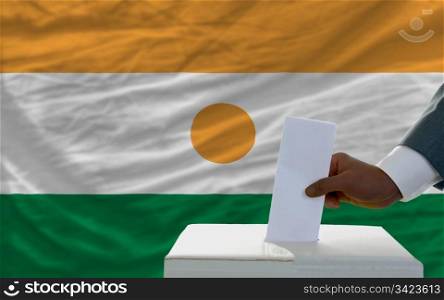 man putting ballot in a box during elections in front of national flag of niger
