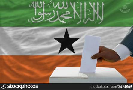 man putting ballot in a box during elections in front of national flag of somaliland