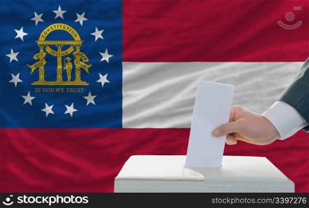man putting ballot in a box during elections in georgia in fornt of flag