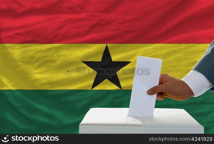 man putting ballot in a box during elections in ghana in fornt of flag