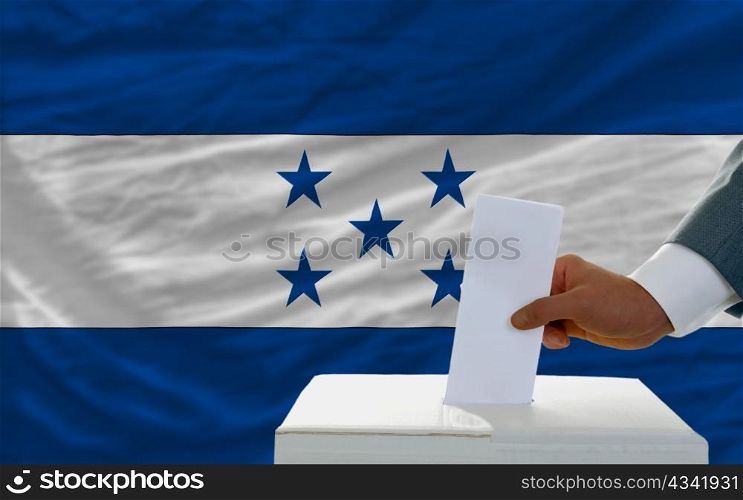 man putting ballot in a box during elections in honduras in fornt of flag