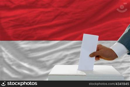 man putting ballot in a box during elections in indonesia in fornt of flag