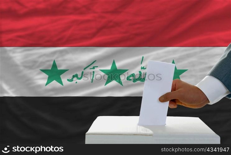 man putting ballot in a box during elections in iraq in fornt of flag