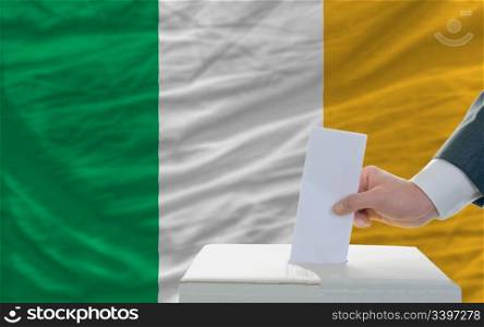man putting ballot in a box during elections in ireland in fornt of flag