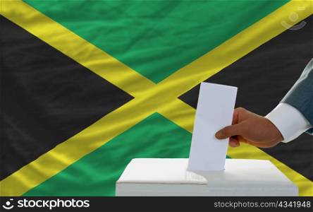 man putting ballot in a box during elections in jamaica in fornt of flag