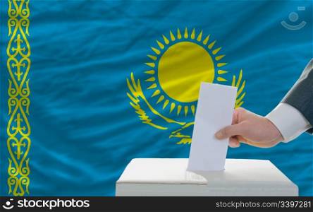 man putting ballot in a box during elections in kazakhstan in fornt of flag