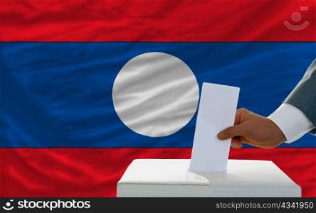 man putting ballot in a box during elections in laos in fornt of flag