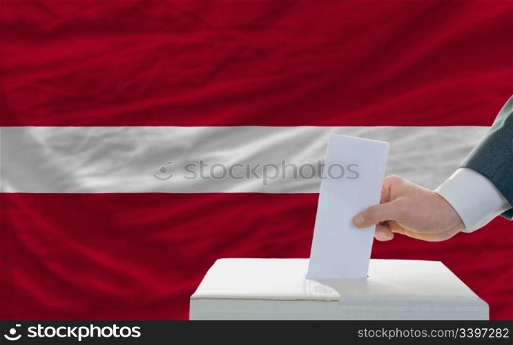 man putting ballot in a box during elections in latvia in front of flag