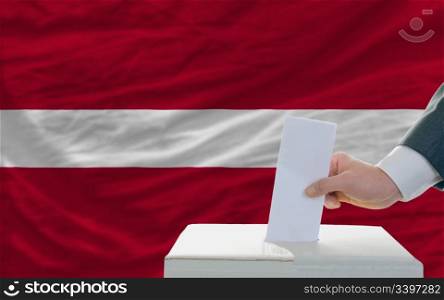 man putting ballot in a box during elections in latvia in front of flag