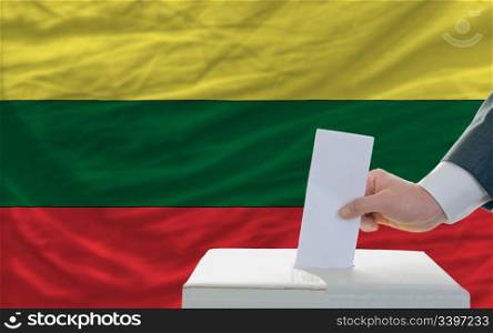 man putting ballot in a box during elections in lithuania in front of flag