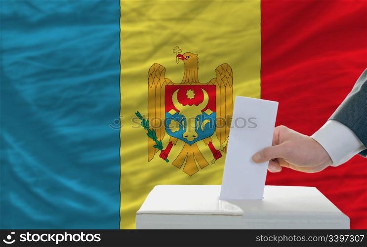 man putting ballot in a box during elections in moldova in front of flag