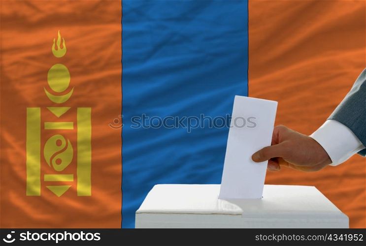 man putting ballot in a box during elections in mongolia in front of flag