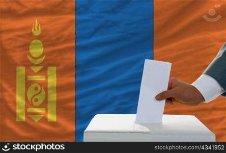 man putting ballot in a box during elections in mongolia in front of flag