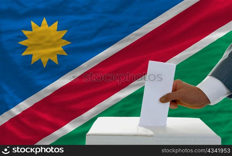man putting ballot in a box during elections in namibia in front of flag