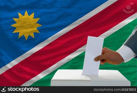 man putting ballot in a box during elections in namibia in front of flag