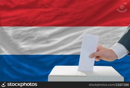 man putting ballot in a box during elections in netherlands in fornt of flag