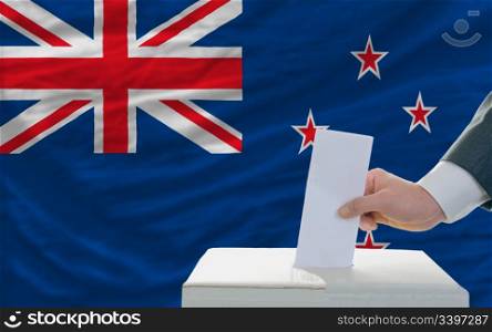 man putting ballot in a box during elections in new zealand in front of flag