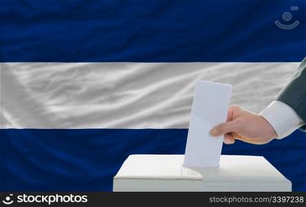 man putting ballot in a box during elections in nicaragua in front of flag