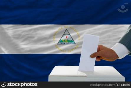 man putting ballot in a box during elections in nicaragua in front of flag