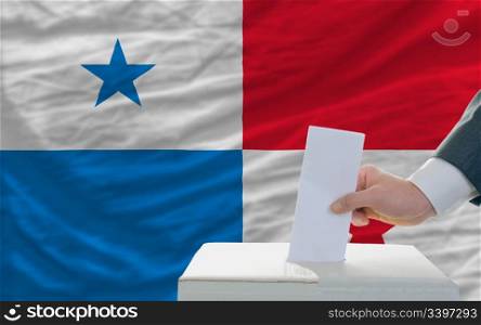 man putting ballot in a box during elections in panama in front of flag
