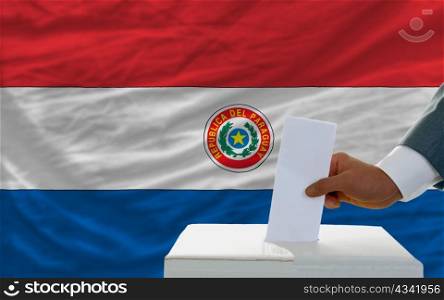 man putting ballot in a box during elections in paraguay in front of flag