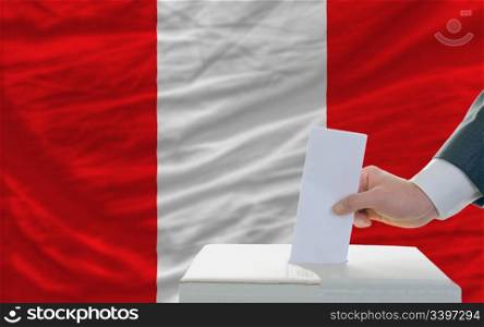 man putting ballot in a box during elections in peru in front of flag