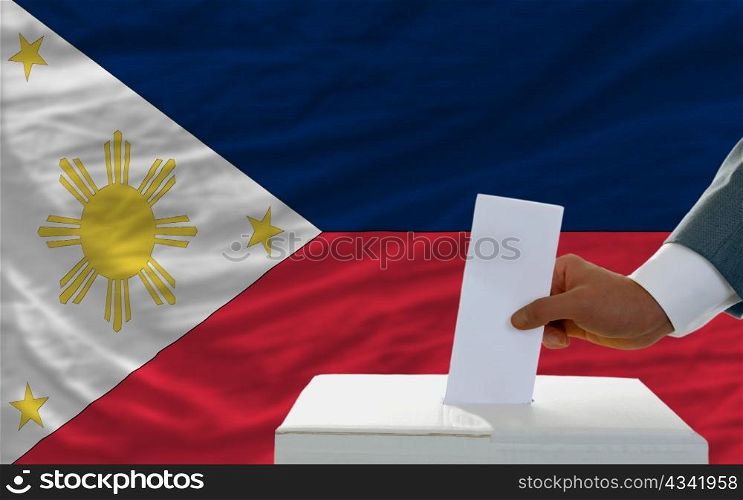 man putting ballot in a box during elections in phillipines in front of flag