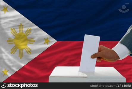 man putting ballot in a box during elections in phillipines in front of flag