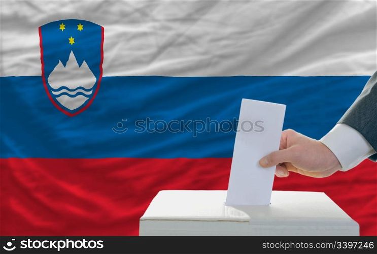 man putting ballot in a box during elections in slovenia in front of flag