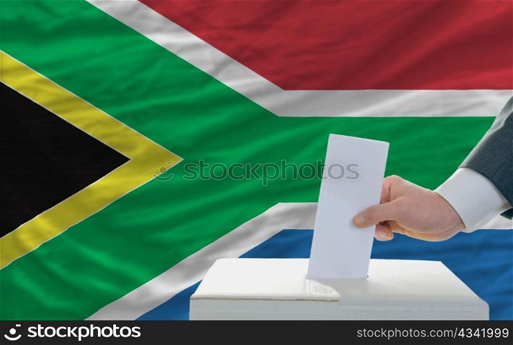 man putting ballot in a box during elections in south africa in front of flag