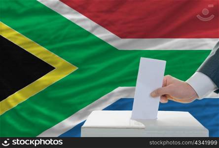 man putting ballot in a box during elections in south africa in front of flag