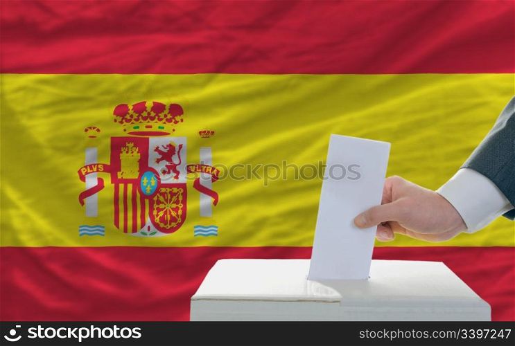man putting ballot in a box during elections in spain in front of flag