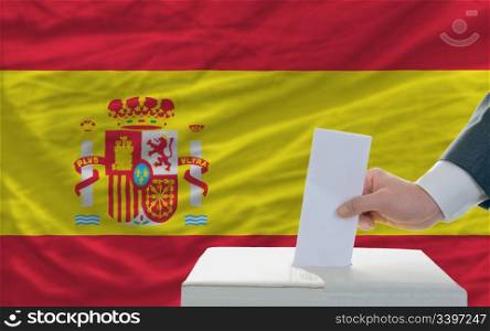 man putting ballot in a box during elections in spain in front of flag