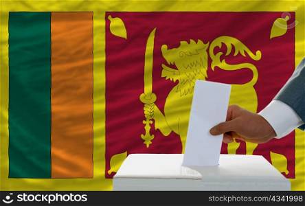 man putting ballot in a box during elections in srilanka in front of flag