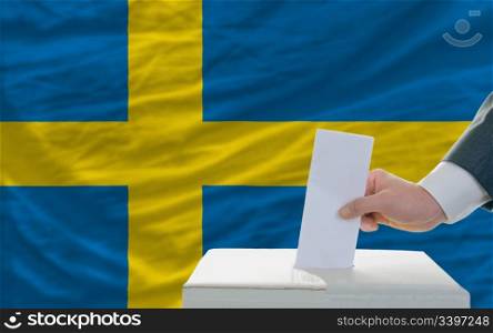 man putting ballot in a box during elections in sweden in front of flag