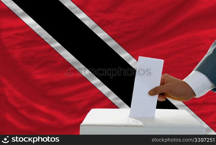 man putting ballot in a box during elections in trinidad tobago in front of flag