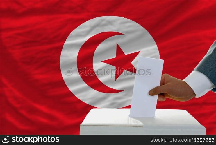 man putting ballot in a box during elections in tunisia in front of flag