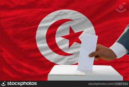 man putting ballot in a box during elections in tunisia in front of flag