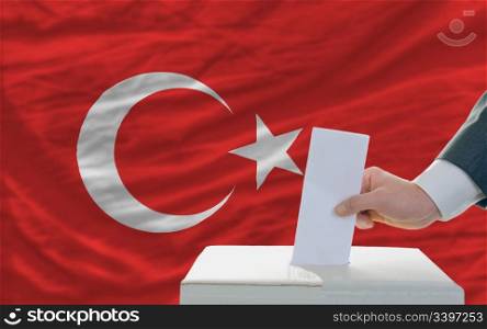 man putting ballot in a box during elections in turkey in front of flag