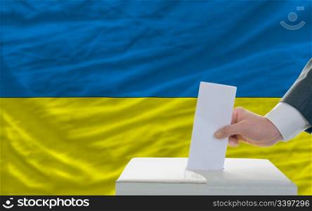 man putting ballot in a box during elections in ukraine in front of flag
