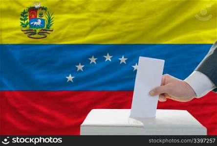 man putting ballot in a box during elections in venezuela in front of flag