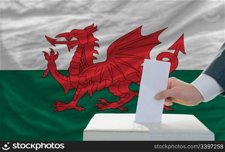 man putting ballot in a box during elections in wales in front of flag