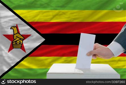 man putting ballot in a box during elections in zimbabwe in front of flag
