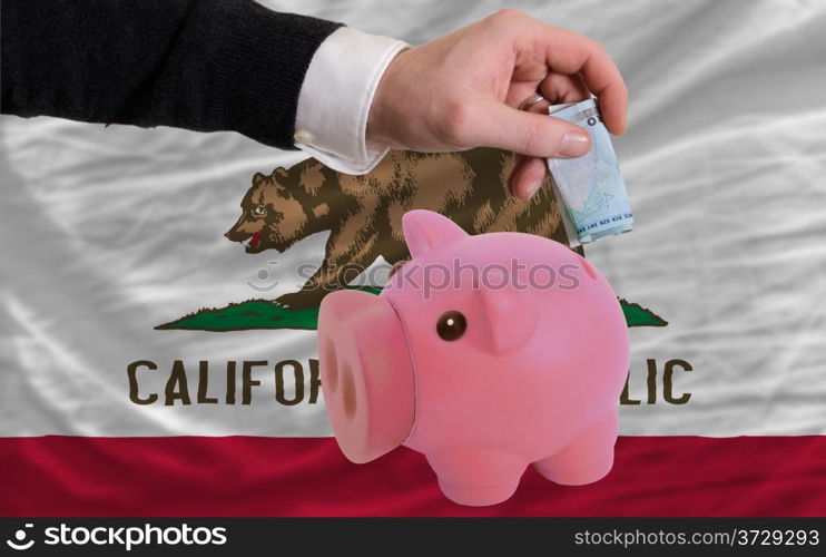 Man putting dollar into piggy rich bank flag of us state of california in foreign currency because of inflation