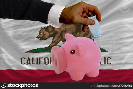 Man putting dollar into piggy rich bank flag of us state of california in foreign currency because of inflation