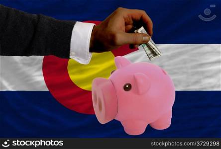 Man putting dollar into piggy rich bank flag of us state of colorado in foreign currency because of inflation