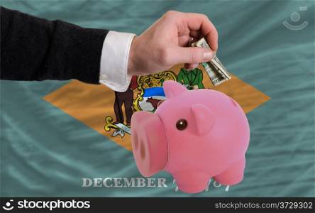 Man putting dollar into piggy rich bank flag of us state of delaware in foreign currency because of inflation